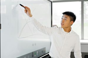 Asian man giving a business presentation using a modern interactive screen in an office setting.