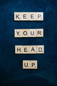 Scrabble tiles spelling 'Keep your head up' on a textured surface.